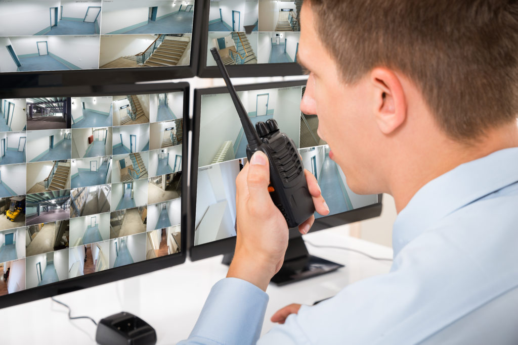 Close-up Of Male Security Guard Talking On Walkie-talkie While Monitoring Multiple CCTV Footage